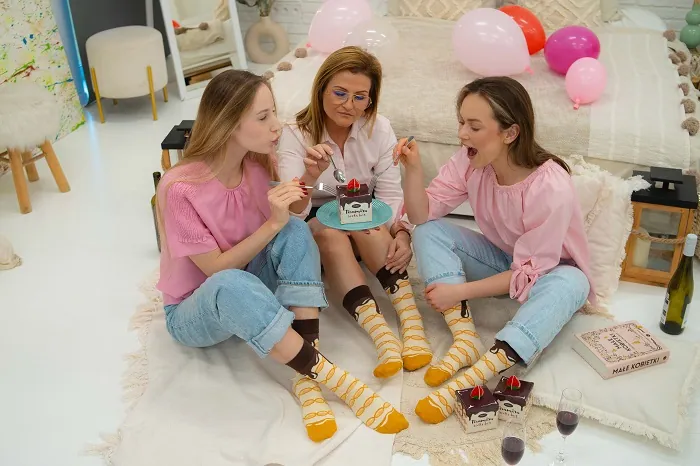 Lächelnde Frauen, die Tiramisu-Socken an ihren Füßen tragen – Socken als Geschenk für Frauen.