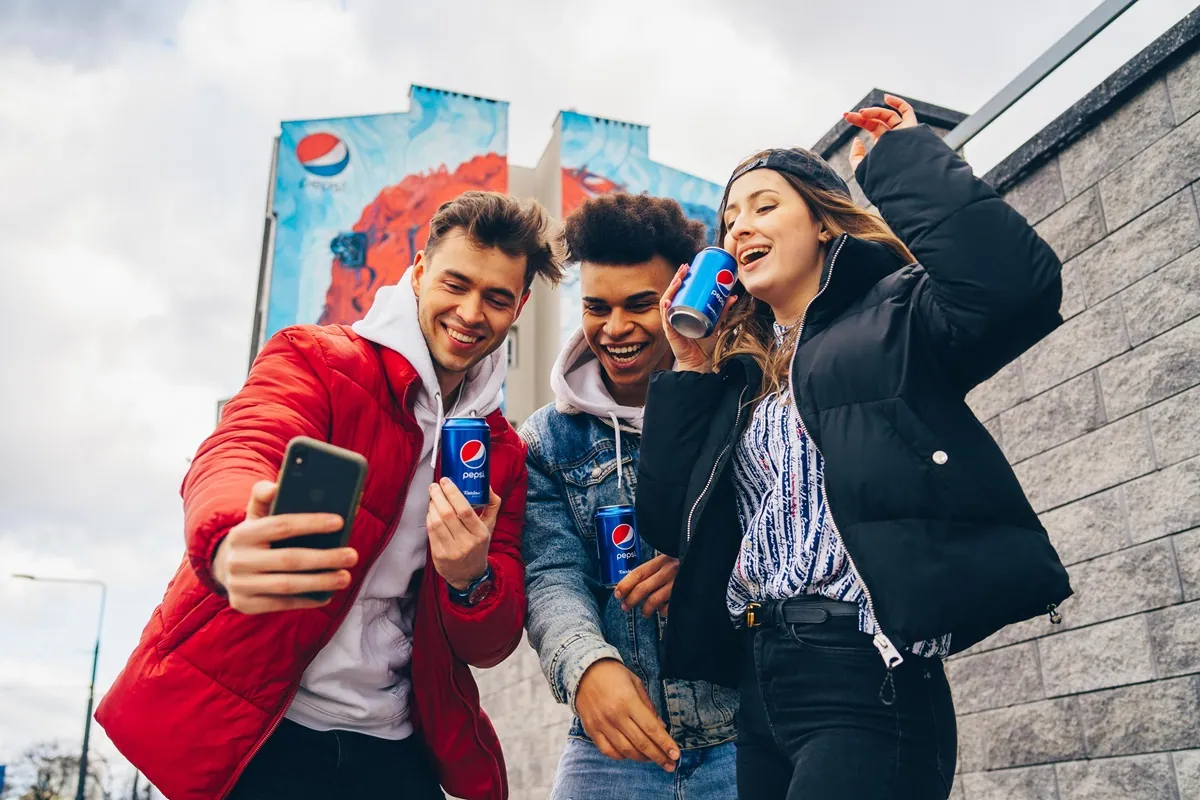 Eine Gruppe von Freunden, die lachen und ein Selfie machen, während sie Socken in einer Pepsi x Rainbow Socks-Dose halten